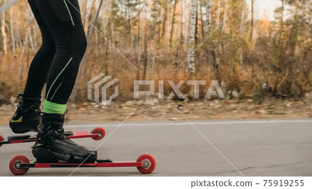 Training an athlete on the roller skaters. Biathlon ride on the roller skis with ski poles, in the helmet. Autumn workout. Roller sport. Training an athlete on the roller skaters. Biathlon ride on the roller skis with ski poles, in the helmet. Autumn workout. Roller sport. 75919255