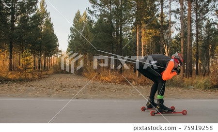 Training an athlete on the roller skaters. Biathlon ride on the roller skis with ski poles, in the helmet. Autumn workout. Roller sport. Training an athlete on the roller skaters. Biathlon ride on the roller skis with ski poles, in the helmet. Autumn workout. Roller sport. 75919258