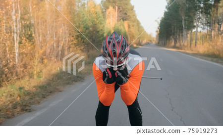 Training an athlete on the roller skaters. Biathlon ride on the roller skis with ski poles, in the helmet. Autumn workout. Roller sport. Training an athlete on the roller skaters. Biathlon ride on the roller skis with ski poles, in the helmet. Autumn workout. Roller sport. 75919273