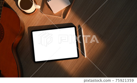 Overhead shot of hipster workplace with digital tablet, notebook, coffee cup and acoustic guitar on wooden floor. Overhead shot of hipster workplace with digital tablet, notebook, coffee cup and acoustic guitar on wooden floor. 75921359