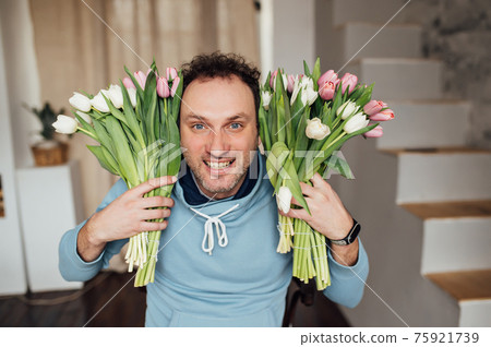 handsome man in a sweatshirt smiles and holds a bouquet of tulips in his hands handsome man in a sweatshirt smiles and holds a bouquet of tulips in his hands 75921739