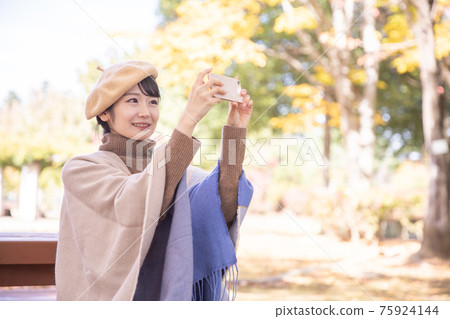A woman taking a picture with a smartphone in an autumn park 75924144