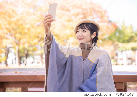 A woman taking a picture with a smartphone in an autumn park A woman taking a picture with a smartphone in an autumn park 75924148