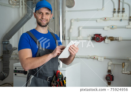 Young worker in a protective suit uses a tablet while checking the boiler equipment in the house. 75924956