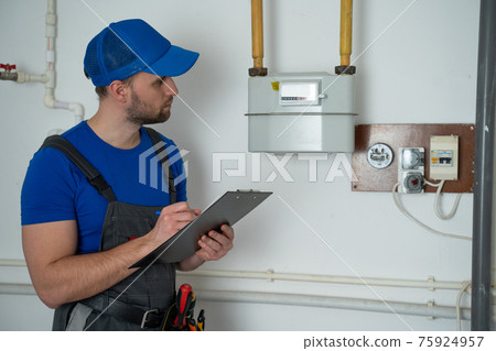 Man in uniform writes down the gas meter reading in a notebook. 75924957