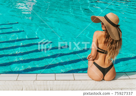 Girl by pool. Happy young sexy woman in bikini swimsuit, sunglasses and straw hat relaxing in blue water. Concept of summer leisure freedom of pleasure. 75927337