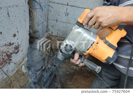 jackhammer in action, pneumatic construction tool, drilling a hole in the concrete wall. jackhammer in action, pneumatic construction tool, drilling a hole in the concrete wall. 75927604