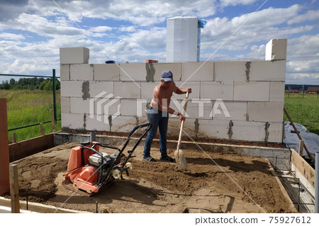 Vibrating plate in use, the worker with the help of a vibrating plate compacts the sand, building a house. Vibrating plate in use, the worker with the help of a vibrating plate compacts the sand, building a house. 75927612