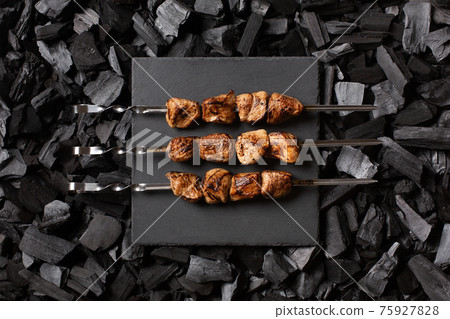 kebab on skewers. Three portions of grilled meat on a stone plate. Charcoal background. Top view. 75927828