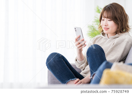 一位女學生在沙發上放鬆,同時在智能手機上閱讀 SNS 消息 一位女學生在沙發上放鬆,同時在智能手機上閱讀 SNS 消息 75928749