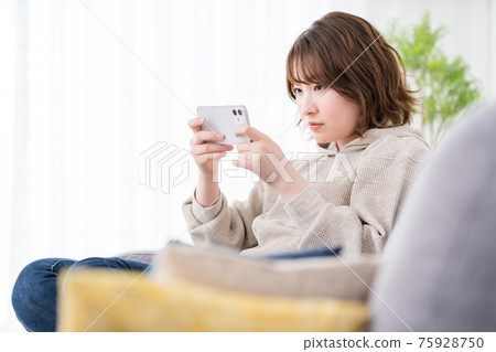 女學生在沙發上玩智能手機網絡遊戲 女學生在沙發上玩智能手機網絡遊戲 75928750