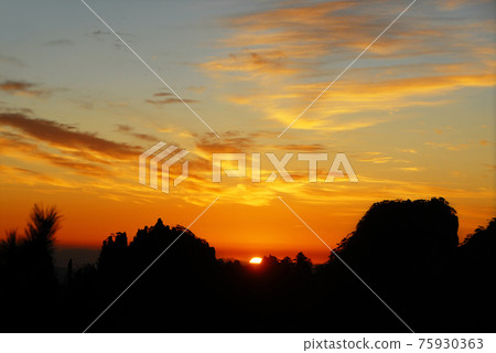 Huangshan Mountain in Anhui Province, China. Sunrise over Huangshan with a colorful sky, clouds and a silhouette of trees on the mountain. Sunrise near the summit of Huangshan Mountain, China. Huangshan Mountain in Anhui Province, China. Sunrise over Huangshan with a colorful sky, clouds and a silhouette of trees on the mountain. Sunrise near the summit of Huangshan Mountain, China. 75930363