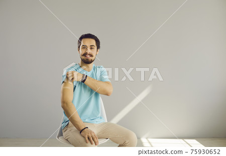 Happy young man sitting on a chair shows his arm after getting a COVID-19 vaccine 75930652