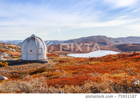 Metal US bunker and autumn greenlandic orange tundra landscape with lakes and mountains in the background, Kangerlussuaq, Greenland 75931187