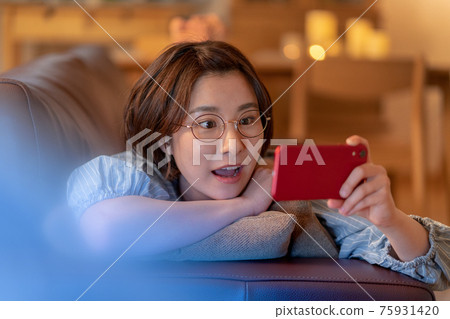 A young woman looking at her smartphone on the sofa in her living room 75931420