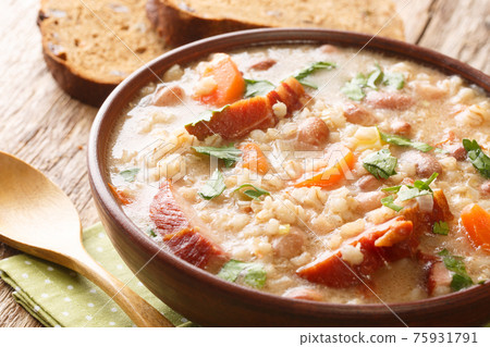 Thick rich barley and bean soup with smoked meat and vegetables close-up in a bowl. horizontal 75931791