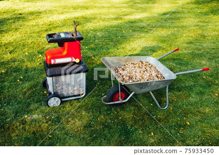 garden chipper, electric shredder (mulcher) with wheelbarrow full of wooden mulch, green grass background 75933450