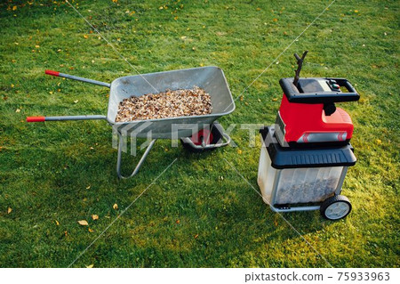 garden chipper, electric shredder (mulcher) with wheelbarrow full of wooden mulch, green grass background 75933963