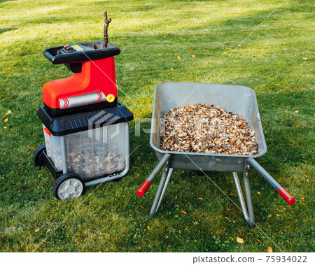 garden chipper, electric shredder (mulcher) with wheelbarrow full of wooden mulch, green grass background 75934022