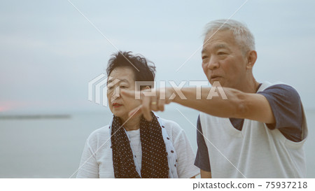 Asian senior elder couple holding hands looking sunset sea ocean together happy retirement life Asian senior elder couple holding hands looking sunset sea ocean together happy retirement life 75937218