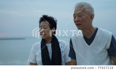 Asian senior elder couple holding hands looking sunset sea ocean together happy retirement life Asian senior elder couple holding hands looking sunset sea ocean together happy retirement life 75937219