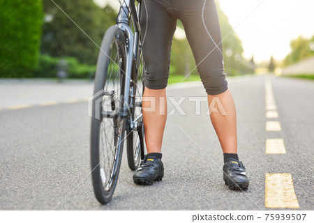 Ready for training. Cropped shot of professional male cyclist wearing cycling shorts and shoes standing with his bike on the road outdoors Ready for training. Cropped shot of professional male cyclist wearing cycling shorts and shoes standing with his bike on the road outdoors 75939507