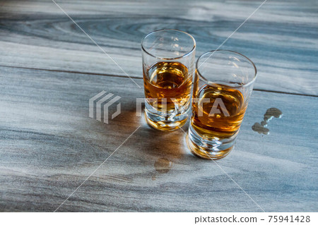 Two shot glasses with whiskey on a wooden background Two shot glasses with whiskey on a wooden background 75941428