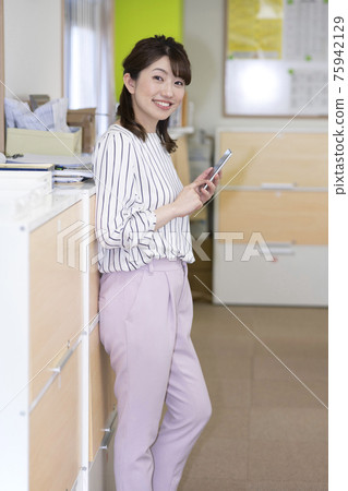 A woman who holds a smartphone and operates it in the office A woman who holds a smartphone and operates it in the office 75942129