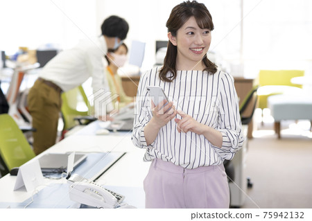 A woman who holds a smartphone and operates it in the office A woman who holds a smartphone and operates it in the office 75942132