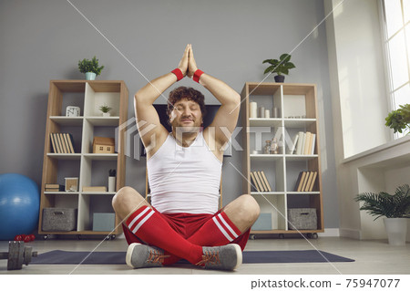 Happy chubby man enjoying meditation and smiling sitting in yoga pose on floor at home Happy chubby man enjoying meditation and smiling sitting in yoga pose on floor at home 75947077