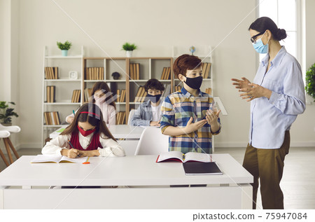 Teacher working with a young student boy should wear a protective mask like the students themselves. Teacher working with a young student boy should wear a protective mask like the students themselves. 75947084