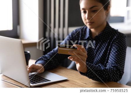 Close up serious Indian woman paying online, holding credit card 75958525