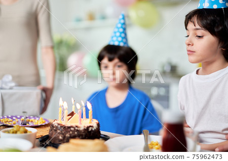 Happy moment. Close up of little hispanic boy looking at birthday cake, making a wish while getting ready for blowing candles. Latin family celebrating birthday together at home Happy moment. Close up of little hispanic boy looking at birthday cake, making a wish while getting ready for blowing candles. Latin family celebrating birthday together at home 75962473