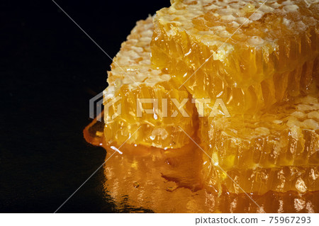 Golden pieces of fresh honeycomb with drops of honey on dark background Golden pieces of fresh honeycomb with drops of honey on dark background 75967293