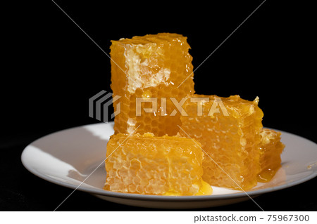 Yellow honey comb slice. Plate with fresh honeycombs and honey on black Yellow honey comb slice. Plate with fresh honeycombs and honey on black 75967300