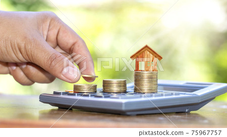 The hand that is holding the coin and free it on the coin stack includes the house model on the coin and a calculator. The hand that is holding the coin and free it on the coin stack includes the house model on the coin and a calculator. 75967757