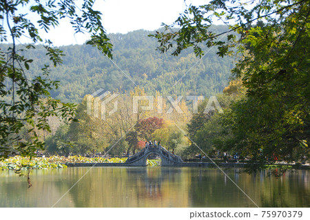 Hongcun Ancient Town in Anhui Province, China. Landscape view of the stone bridge crossing Nanhu Lake in Hongcun with fall backdrop. Framed by foreground branches. The ancient town of Hongcun in China 75970379