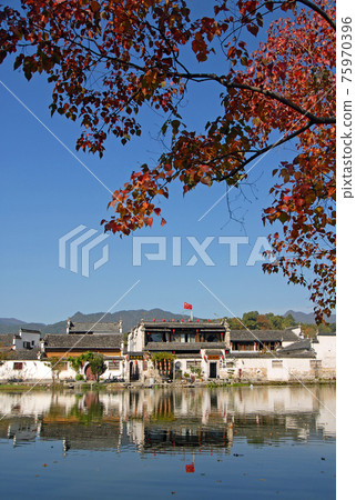 Hongcun Ancient Town in Anhui Province, China. The old town across Nanhu Lake in Hongcun with blue sky and red tree. Ancient town of Hongcun in China with old buildings, and lake in fall. Hongcun Ancient Town in Anhui Province, China. The old town across Nanhu Lake in Hongcun with blue sky and red tree. Ancient town of Hongcun in China with old buildings, and lake in fall. 75970396