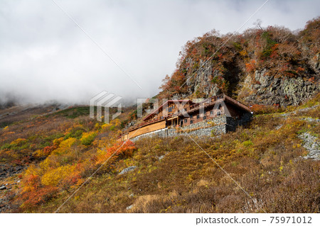 Karasawa Hut on the hillside of Mt. Kitahotaka. Autumn leaves and yellow leaves of Karasawa Cirque, the largest in Japan at an altitude of 2,300 m in Azumi, Matsumoto City. cloud. Karasawa Hut on the hillside of Mt. Kitahotaka. Autumn leaves and yellow leaves of Karasawa Cirque, the largest in Japan at an altitude of 2,300 m in Azumi, Matsumoto City. cloud. 75971012