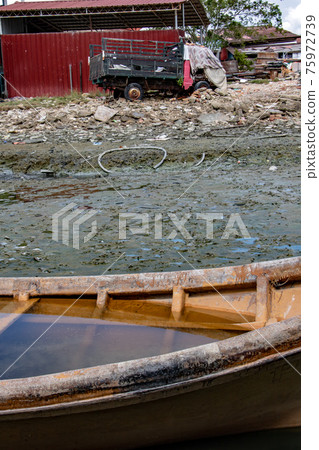 Flooded ship in mud in dry lagoon with damaged lorry in ruins on a background.  75972739