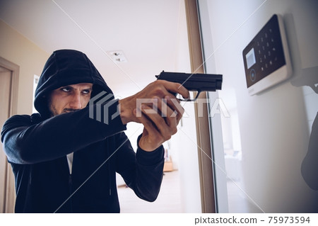 Burglar in hood holding a gun in hand breaking into the house. 75973594