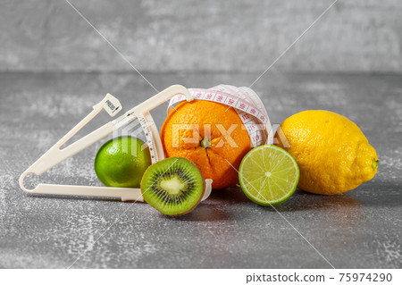 An orange wrapped with a measuring tape and a caliper surrounded by fresh fruits 75974290