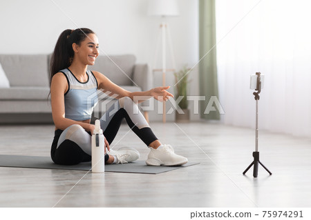 Pretty woman sitting on yoga mat, having video call Pretty woman sitting on yoga mat, having video call 75974291