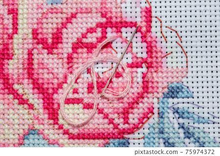 Close-up on a sewing needle with thread lying on top of a cross-stitched canvas Close-up on a sewing needle with thread lying on top of a cross-stitched canvas 75974372