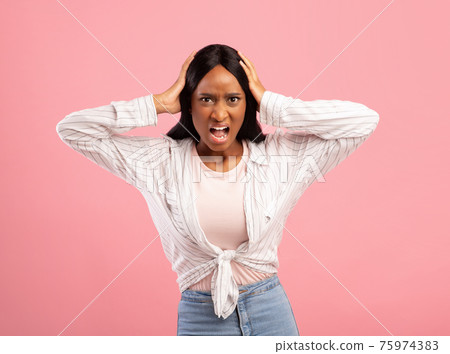 Furious black woman screaming and holding her head on pink studio background 75974383