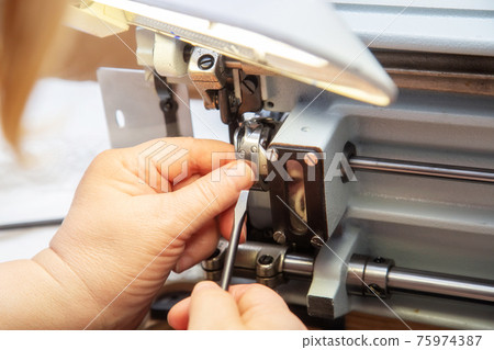 Female hands with a screwdriver repair the shuttle of the sewing machine. Female hands with a screwdriver repair the shuttle of the sewing machine. 75974387