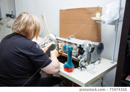 Woman tilts the sewing machine on its side and reads the repair instructions Woman tilts the sewing machine on its side and reads the repair instructions 75974388