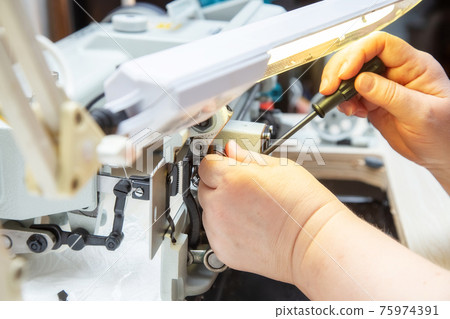Female hands with a screwdriver repair the shuttle of the sewing machine. 75974391