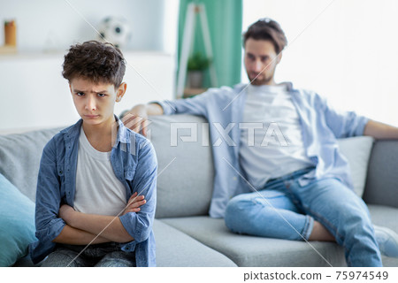 Family generations conflict. Upset boy and father not talking after quarrel, son and dad sitting on couch separately Family generations conflict. Upset boy and father not talking after quarrel, son and dad sitting on couch separately 75974549