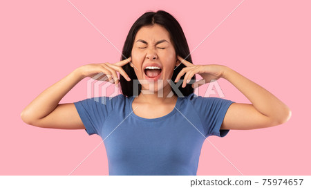 Angry asian woman plugging her ears with fingers and screaming Angry asian woman plugging her ears with fingers and screaming 75974657